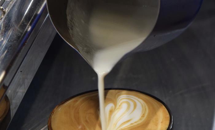 A close up of a barista's hands as they pour the last of the milk into a latte cup.